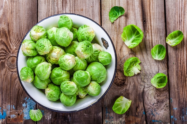 A bowl of uncooked Brussels sprouts on top of a wooden board