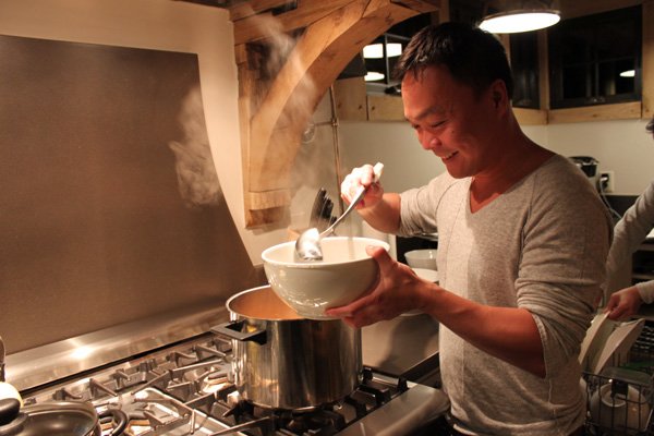 Asian cook spooning Vietnamese pho ga soup into a large white soup bowl over a hot stove