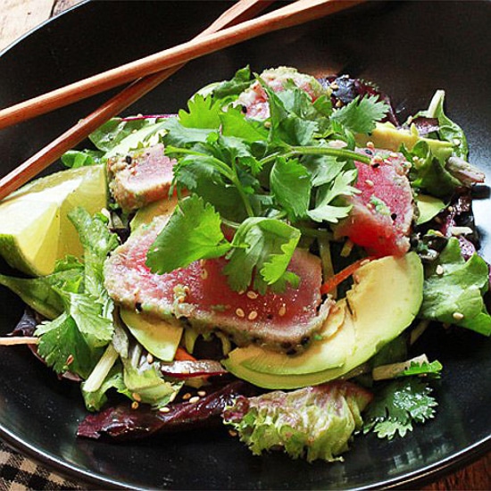 Seared ahi tuna on a bed of greens in a black bowl with wooden chopsticks on the side.