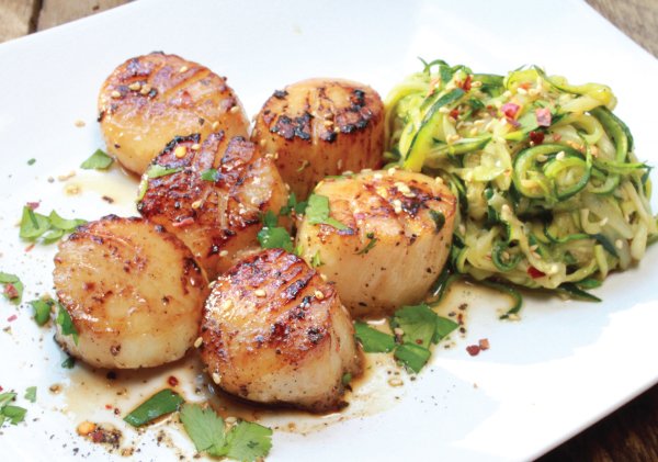 Pan Seared Asian Scallops on a white plate with zucchini noodles on the side.