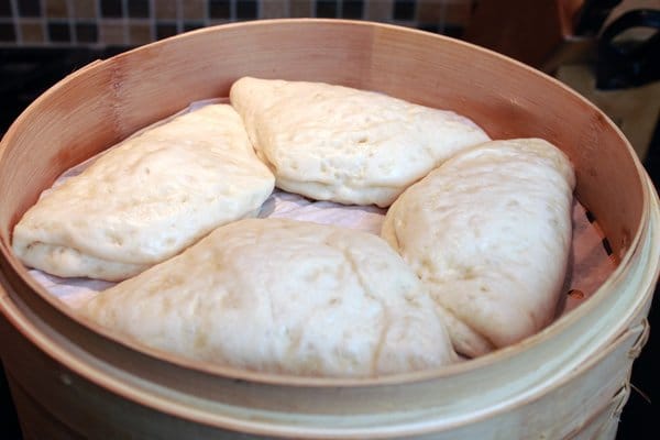 Bao buns in a bamboo steamer with the lid off.