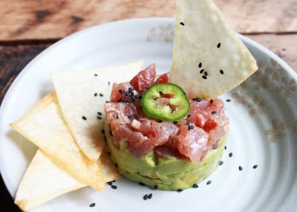 Vibrant Ahi tuna napoleon tower topped with jalapeño slices on a plate with sesame chips on the side.