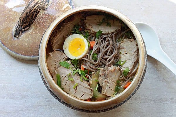 pork soup and soba noodles in a ceramic soup bowl topped with a soft boiled egg with a white spoon on the side
