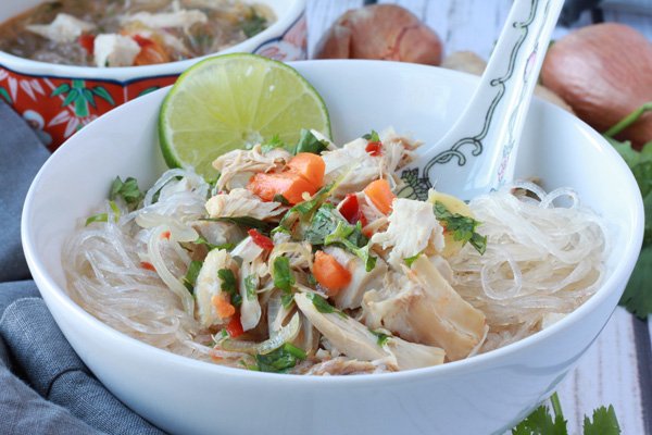 turkey noodle soup A white bowl filled with Asian turkey noodle soup with rice noodles and chunks of turkey on top with an Asian soup spoon inserted and a slice of lime.