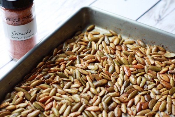 a baking tray with toasted Sriracha pumpkin seeds on a white board