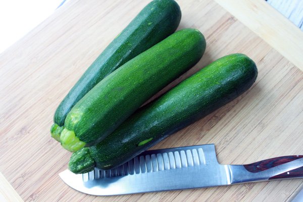 2 zucchinis on a wooden cutting board and a cutting knife