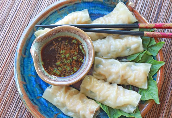 Steamed Vietnamese rolls on a round blue plate with a small bowl of dipping sauce on the side on top of a wooden table top.