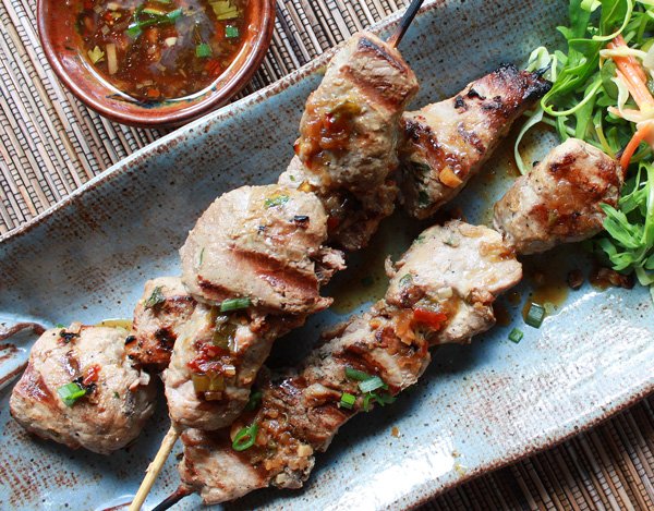 Vietnamese pork tenderloin skewers on a long blue platter with a side salad and dipping sauce on the side.