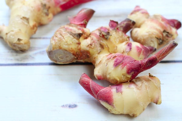 Pieces of fresh ginger bulbs on a white plank wooden board.