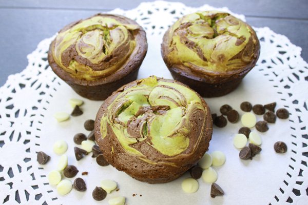 Three matcha cheesecake muffins with white and dark chocolate chips on a white doily.