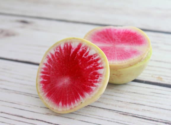 Vibrant rainbow radish sliced on top of a white board.
