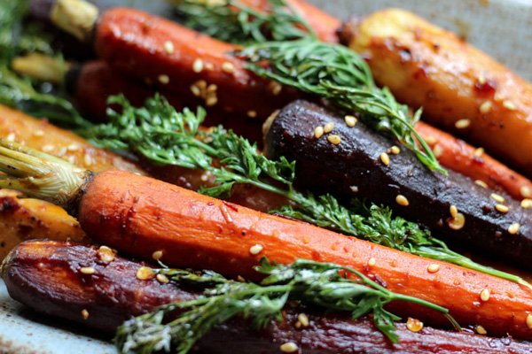 Close up shot of colorful roasted rainbow carrots with tops on garnished with sesame seeds.