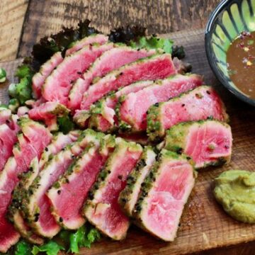 seared tuna slices on a wooden cutting board with a side of dipping sauce and wasabi