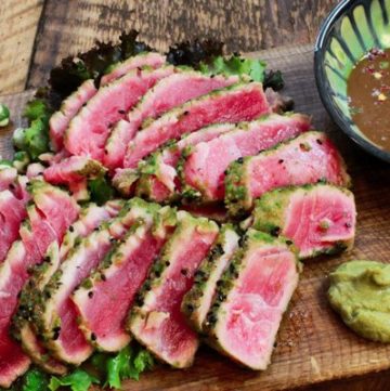 seared tuna slices on a wooden cutting board with a side of dipping sauce and wasabi