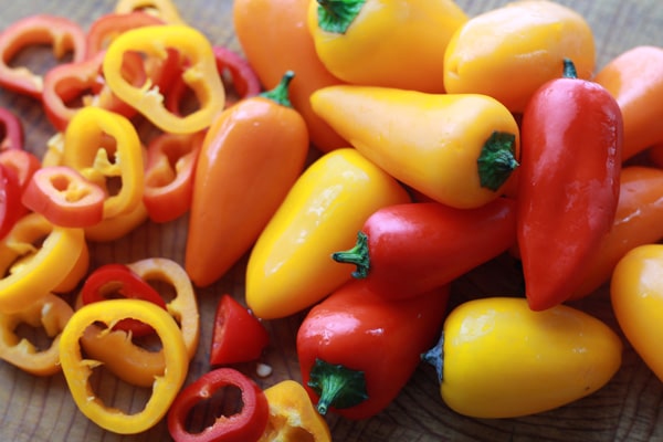 mini bell peppers Orange, yellow and red mini bell peppers with sliced peppers on the side on top of a wooden cutting board.