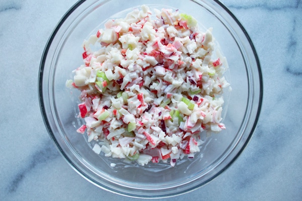 california crab mix A clear glass mixing bowl filled with a crab meat salad on top of a marble surface.