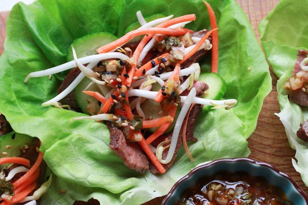 grilled flank steak lettuce cups Grilled flank steak lettuce cups with a side of nuoc cham sauce in a dark blue bowl on top of a wooden board.
