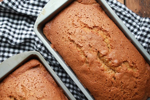 pumpkin bread Two baked pumpkin breads in aluminum loaf pans on top of a black and white checkered napkin.
