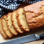 Sliced pumpkin bread on a wooden board with a bread knife and checkered napkin on the side.
