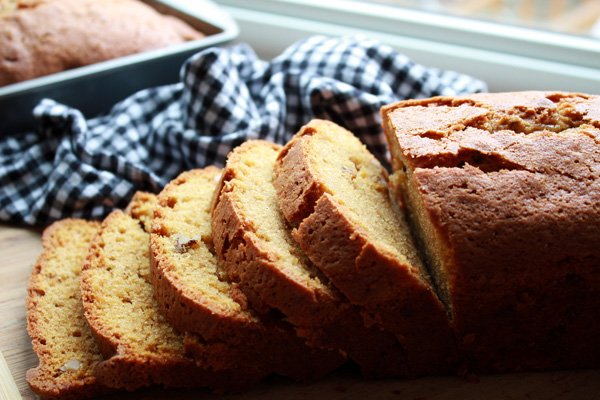 A sliced loaf of Five Spice Pumpkin Bread on a board with a checkered napkin on the side.
