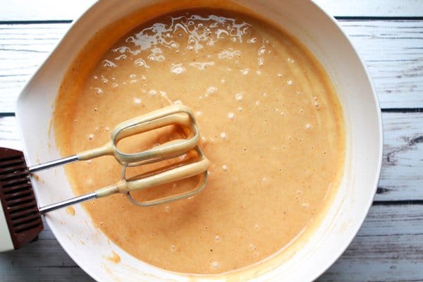 pumpkin bread A white mixing bowl filled with pumpkin bread batter with mixing beaters on the side on top of a white wooden plank board.