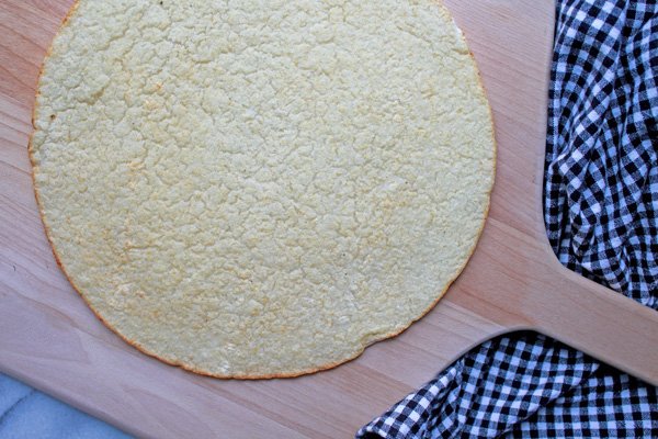 Trader Joe's Cauliflower Pizza Crust A baked Trader Joe's Cauliflower Pizza Crust right out of the oven on top of a wooden pizza peel with a black and white checkered napkin on the side.