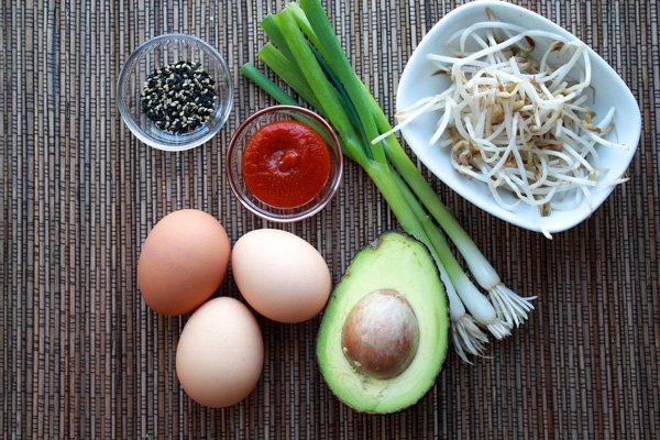 bao buns Ingredients for making steamed bao buns including avocado, eggs, green onions, sriracha sauce and bean sprouts, on top of a textured placemat.