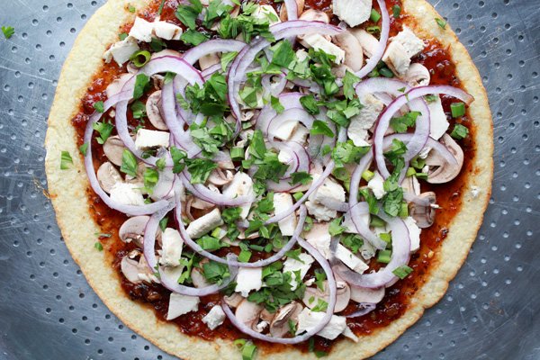 Korean BBQ Cauliflower Pizza Korean BBQ Cauliflower Pizza pie ready to be put in the oven topped with veggies and fresh herbs on top of a silver pizza tray.
