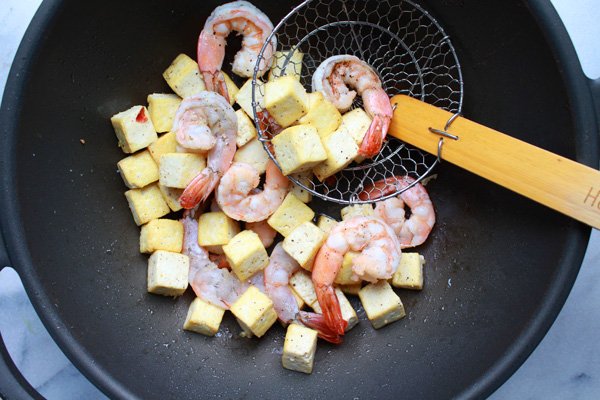 shrimp and tofu Shrimp and tofu cubes being fried in a wok with a slotted wire spoon inserted inside.