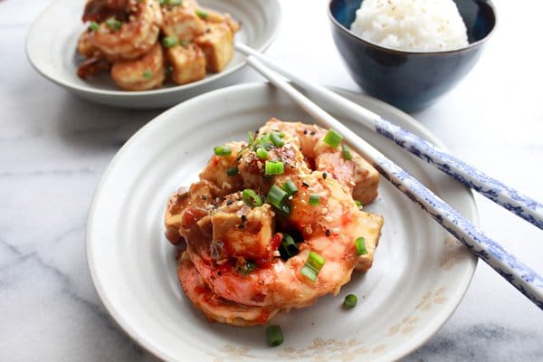 Two white bowls of General Tso's Shrimp and Tofu with chopsticks and a bowls of white rice on the side.