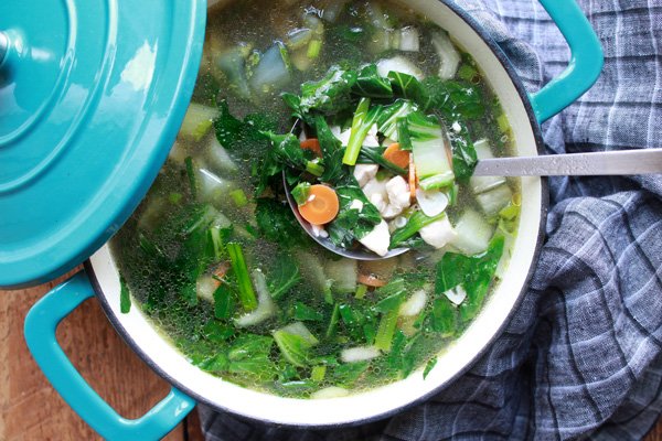 a large blue pot of Thai Clear Soup with a ladle inserted in the pot placed on top of a wooden board