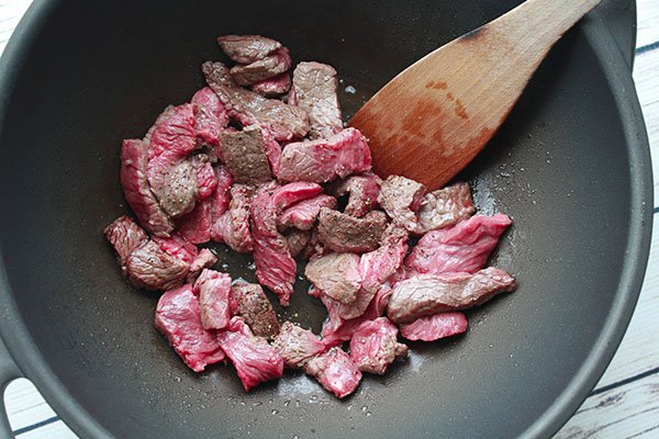stir-fry beef Sliced sirloin beef being stir-fried in a large wok with a wooden spoon inserted.