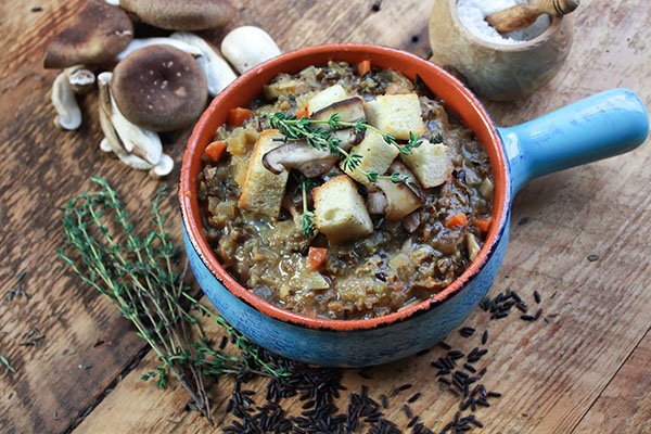 wild mushroom soup A blue soup bowl filled with chunky wild rice mushroom soup topped with fresh croutons and sprigs of thyme on top of a wooden board with shiitake mushrooms on the side.
