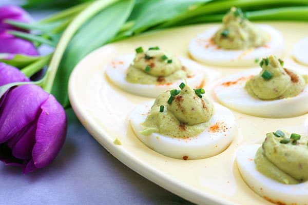 avocado deviled eggs avocado deviled eggs in an egg tray with purple tulips along side