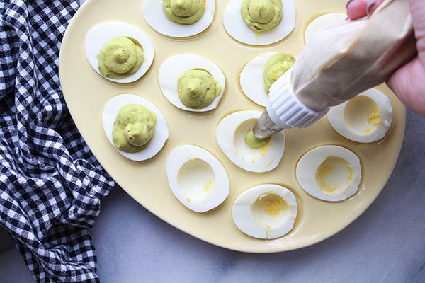 avocado deviled eggs being piped in the whites of the eggs