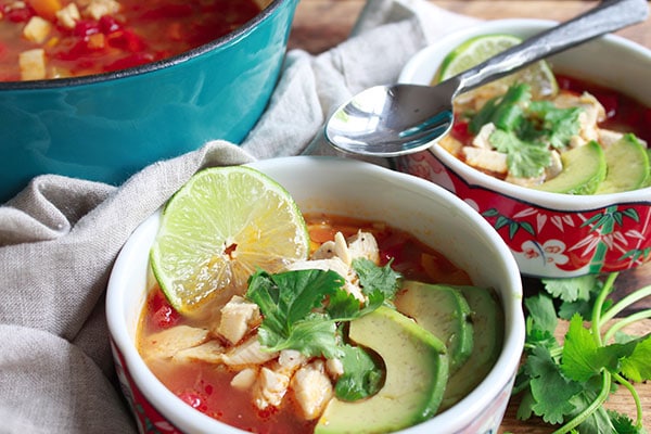 two bowls of chicken tortilla soup with a spoon and a large stock pot