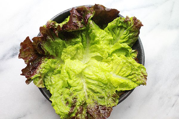 garden lettuce Pieces of lettuce leave in a black bowl on top of a marble surface.