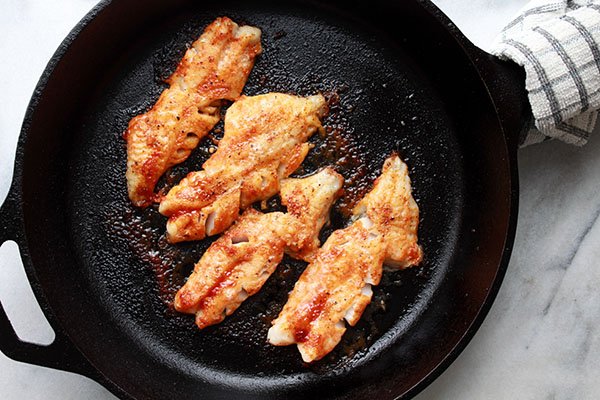 Seared Gochujang-Glazed Redfish Four filets of Gulf of Maine Redfish being seared in a cast iron skillet with a kitchen wrapped around the handle on top of a marble surface.