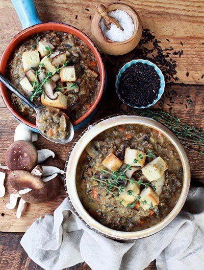 Two bowls of mushroom soup on top of a wooden board with shiitake mushrooms, black sesame seeds and a bowl of salt on the side.