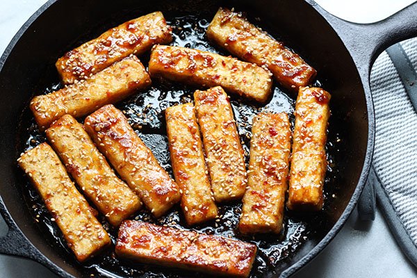 seared tofu strips Golden-brown sesame seared tofu strips searing up in a cast iron skillet.