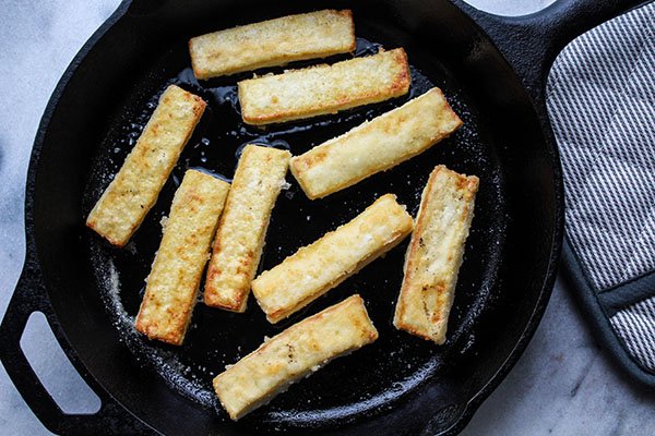 seared tofu strips Crispy golden-brown tofu strips searing up in cast iron skillet with an oven mitt on the side!