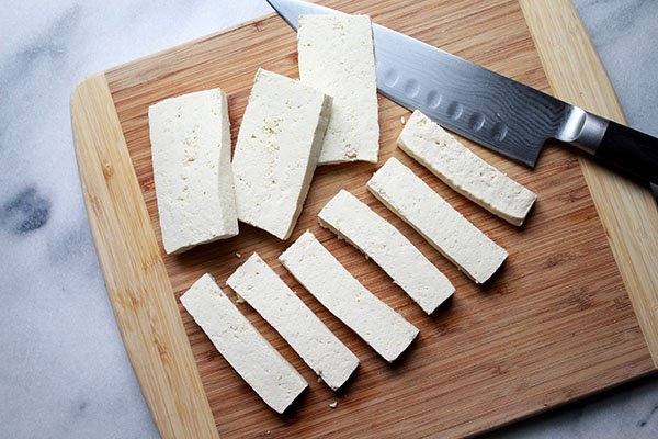 tofu strips on a cutting board with a chefs knife on the side