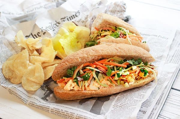 A lobster banh mi sandwich on top of a newspaper with potato chips on the side.