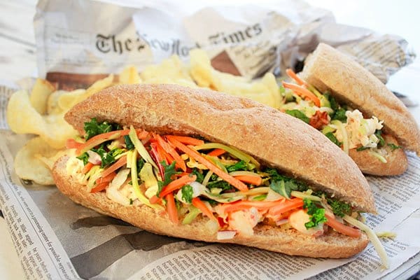 A lobster banh mi sandwich on top of a newspaper with potato chips on the side.