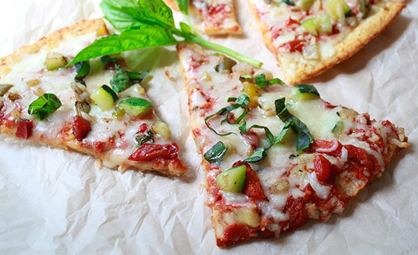 Roasted veggie cauliflower pizza slices on top of parchment paper topped with a sprig of fresh basil.