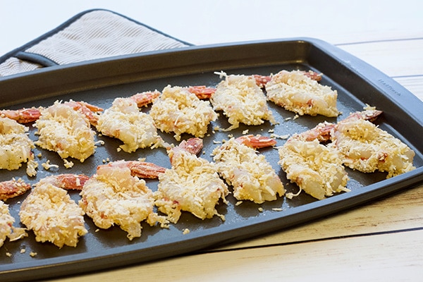 gluten-free baked coconut shrimp A baking tray layered with jumbo coconut shrimp ready for the oven, on top of a white wooden board.