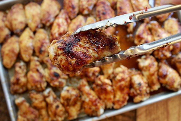 baked Korean chicken wings a pair of tongs holding up a baked Korean chicken wing overhead a baking sheet with chicken wings