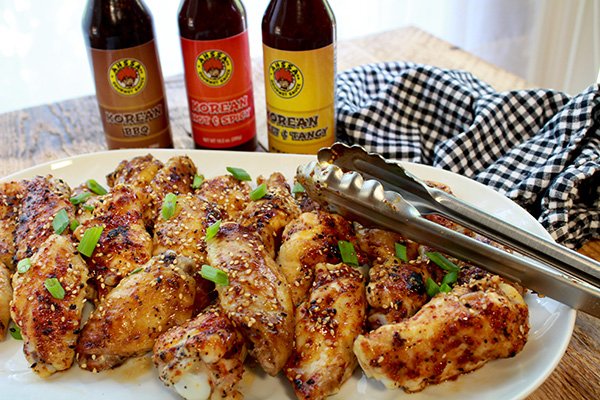 baked Korean chicken wings baked Korean chicken wings on a white platter with tongs and three bottled sauces placed behind