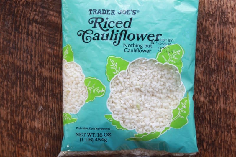Trader Joe's Riced Cauliflower A blue bag of Trader Joe's riced cauliflower placed on top of a wooden board.