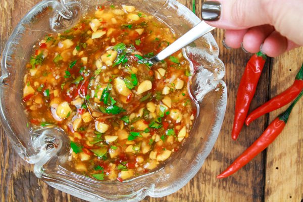 Thai sweet and spicy sauce A glass bowl filled with Thai sweet and spicy sauce with chopped peanuts on top of a wooden board with Thai chili peppers on the side.